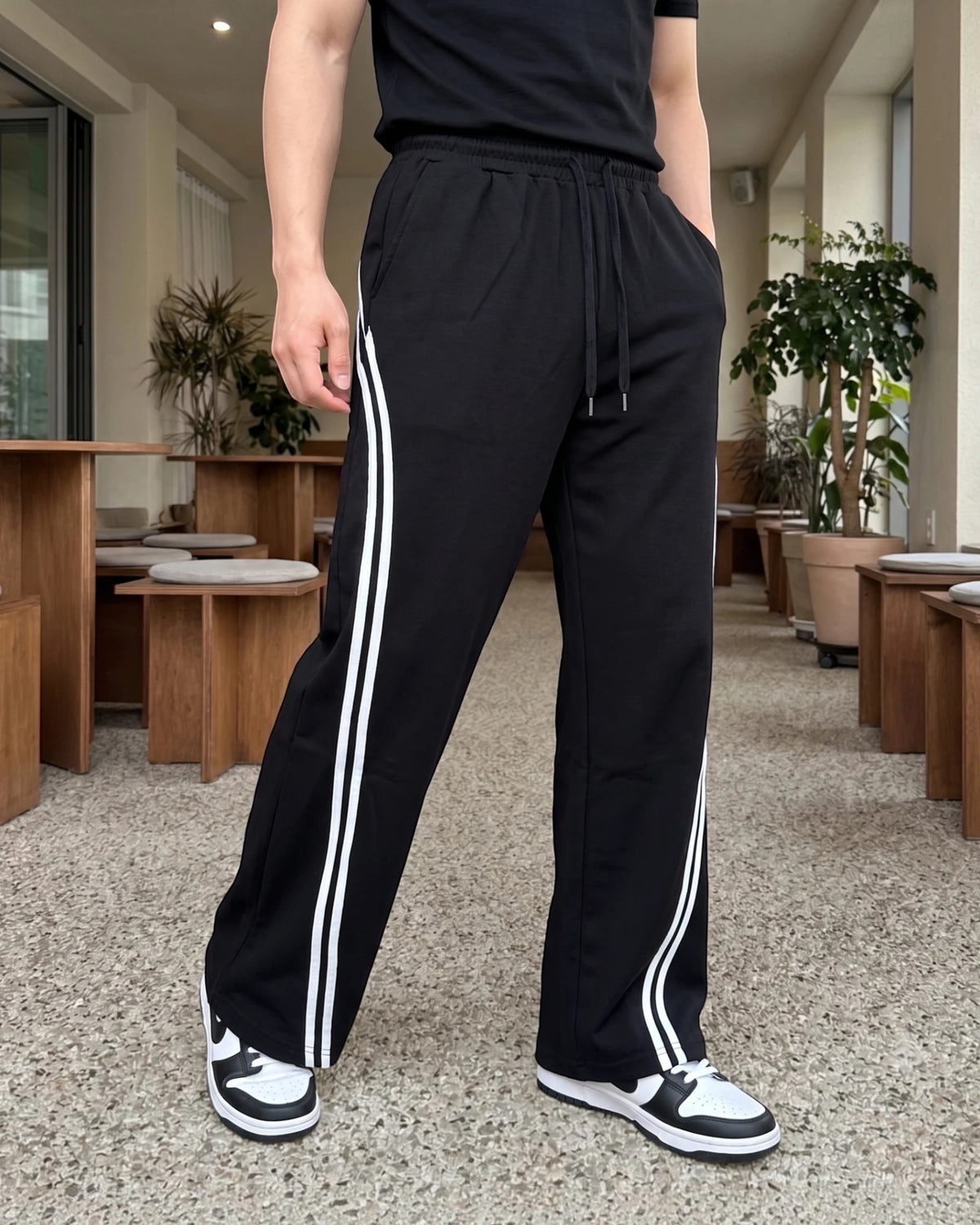 Black wide-leg sweatpants with double white side stripes, front view