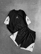 The Black & White Jordan-Inspired Two Piece Set – Men’s Casual Sportswear Outfit includes a matching black T-shirt and shorts with white panels and a basketball player logo, shown flat on a gray textured surface.