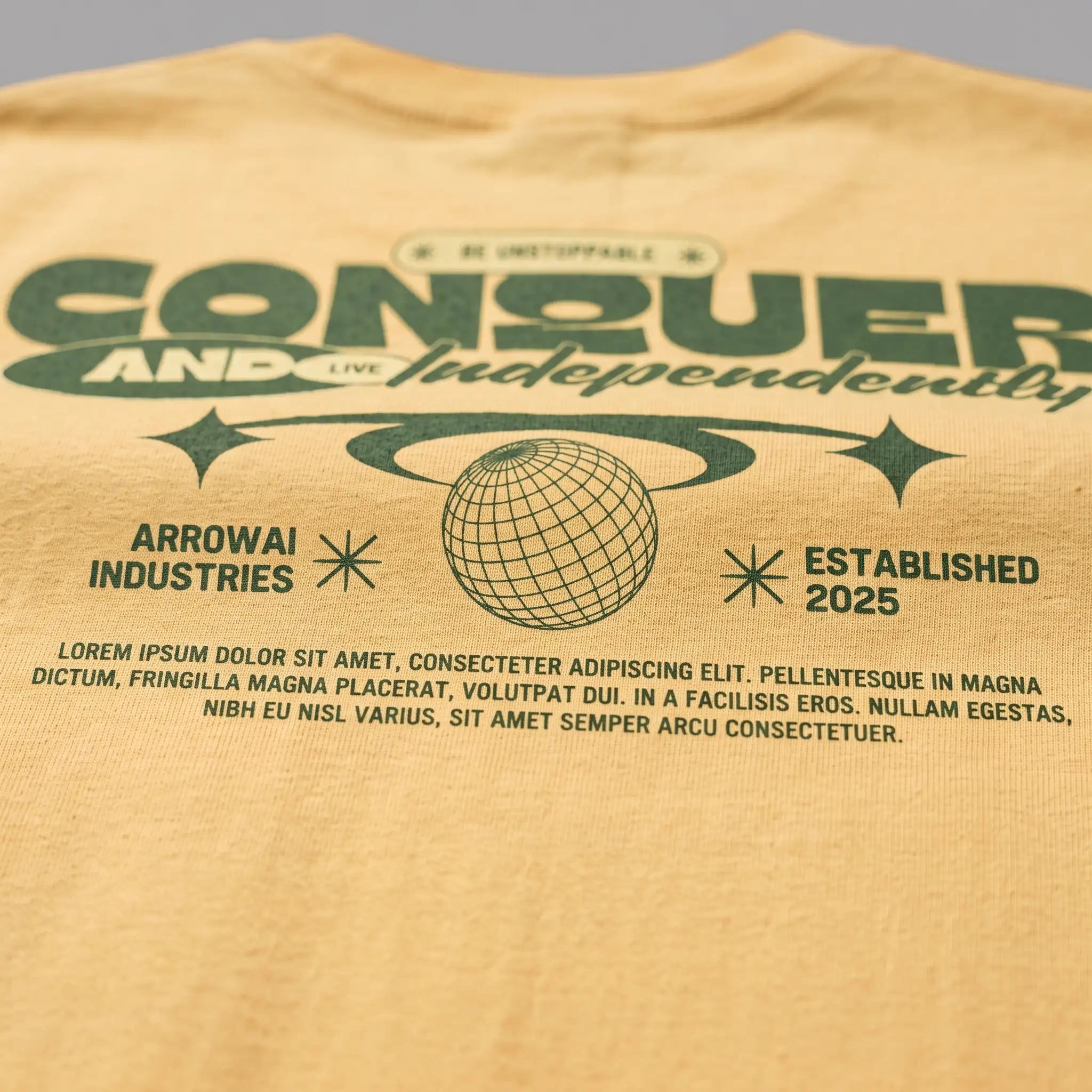 Close-up back print of a pastel yellow streetwear graphic tee featuring retro green Conquer lettering and globe design.