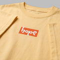 Close-up detail of a pale yellow graphic t-shirt featuring an orange rectangular 'hope' box logo print on the chest.