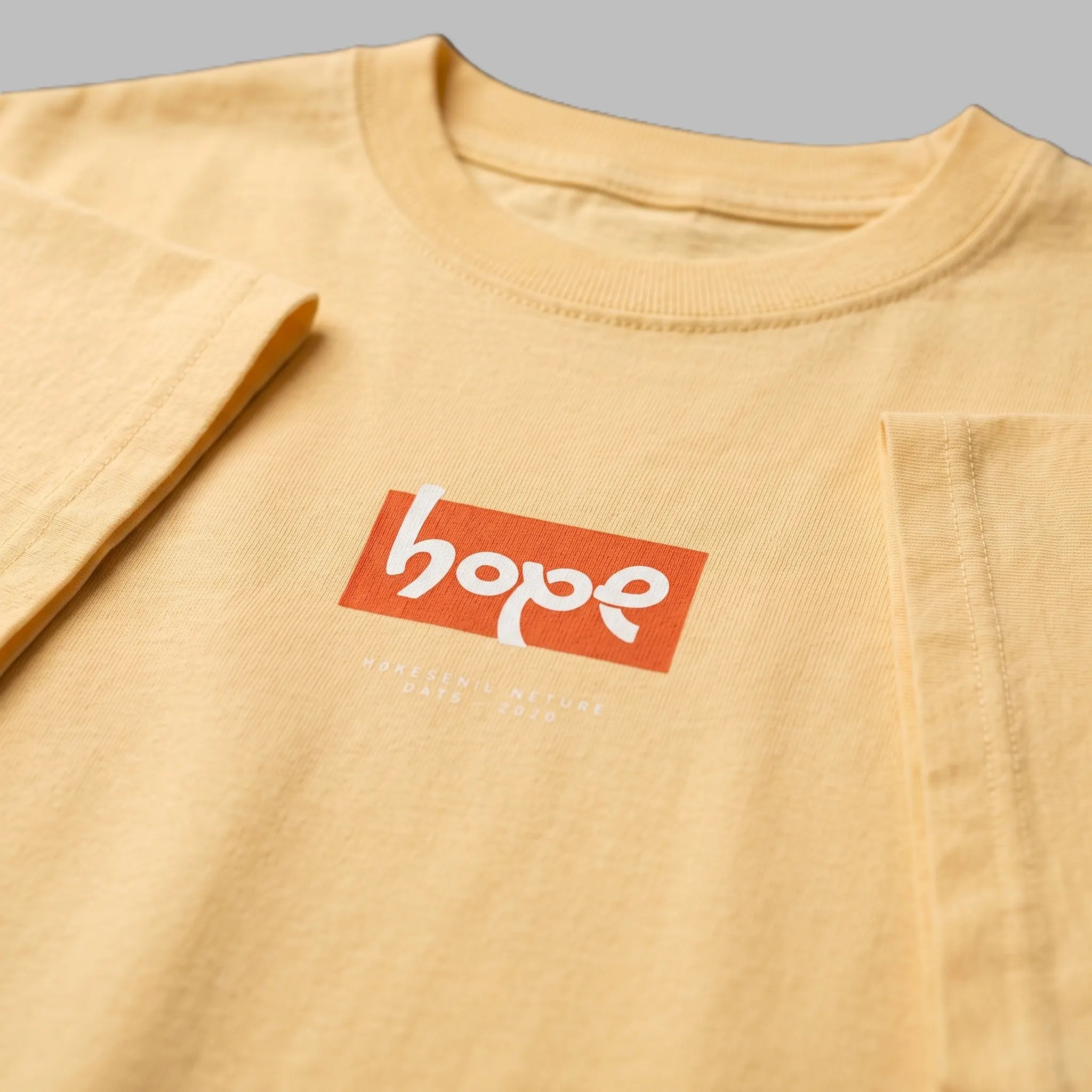Close-up detail of a pale yellow graphic t-shirt featuring an orange rectangular 'hope' box logo print on the chest.