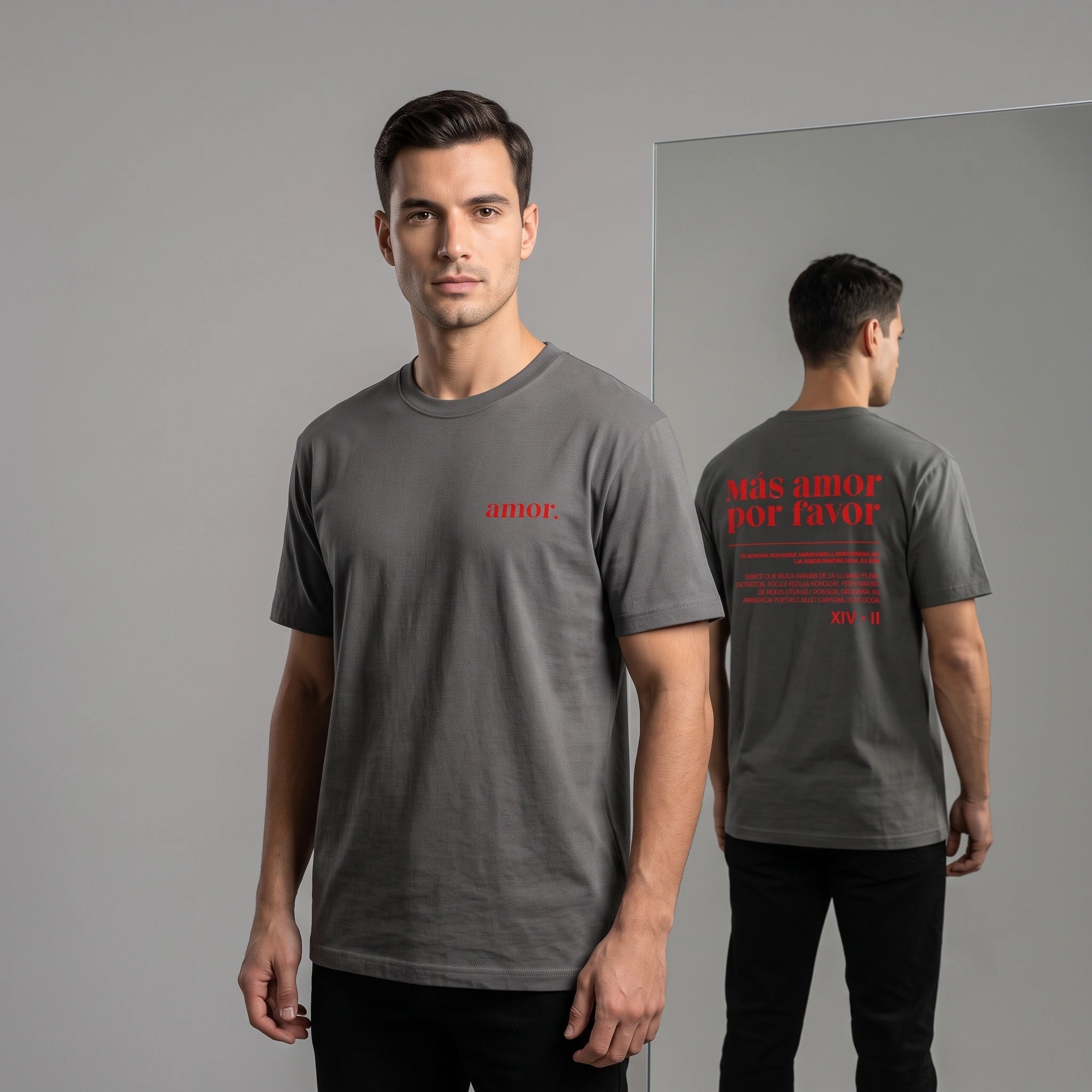 Studio shot showcasing front and back views of a faded black heavyweight garment-dyed t-shirt on a male model. The front view has small red "amor." text. The back view, a mirror reflection, features larger red text: "más amor por favor" with additional smaller text details and the date "XIV • II".