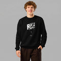 A smiling male model with curly brown hair standing against a grey background with one hand in his pocket. He is wearing a black crewneck sweatshirt paired with dark brown trousers. The sweatshirt features a white and grey graphic on the chest with the bold text 'RUN', a runner's silhouette across the letters, and 'VIENNA RUNNING CLUB' printed below.