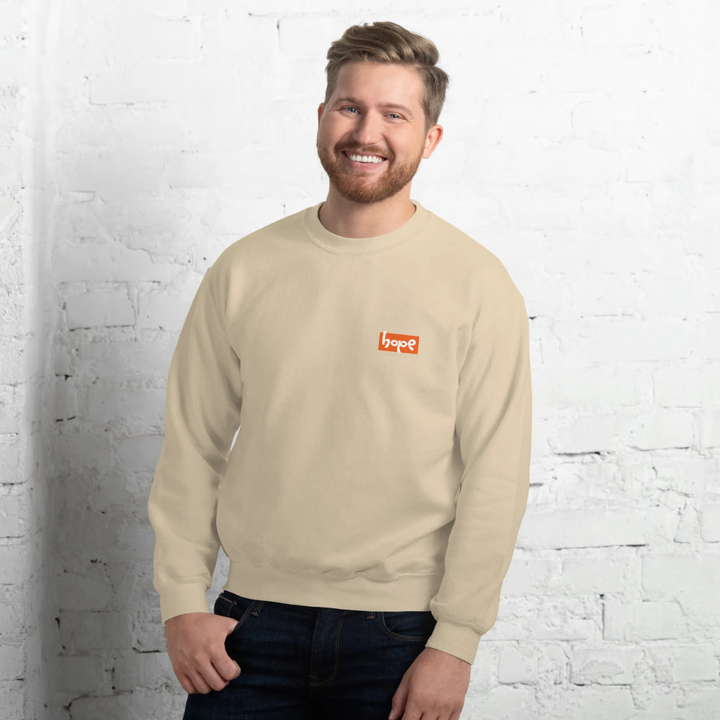 Smiling male model standing against white brick wall wearing sand beige crewneck sweatshirt with orange Hope chest logo front view