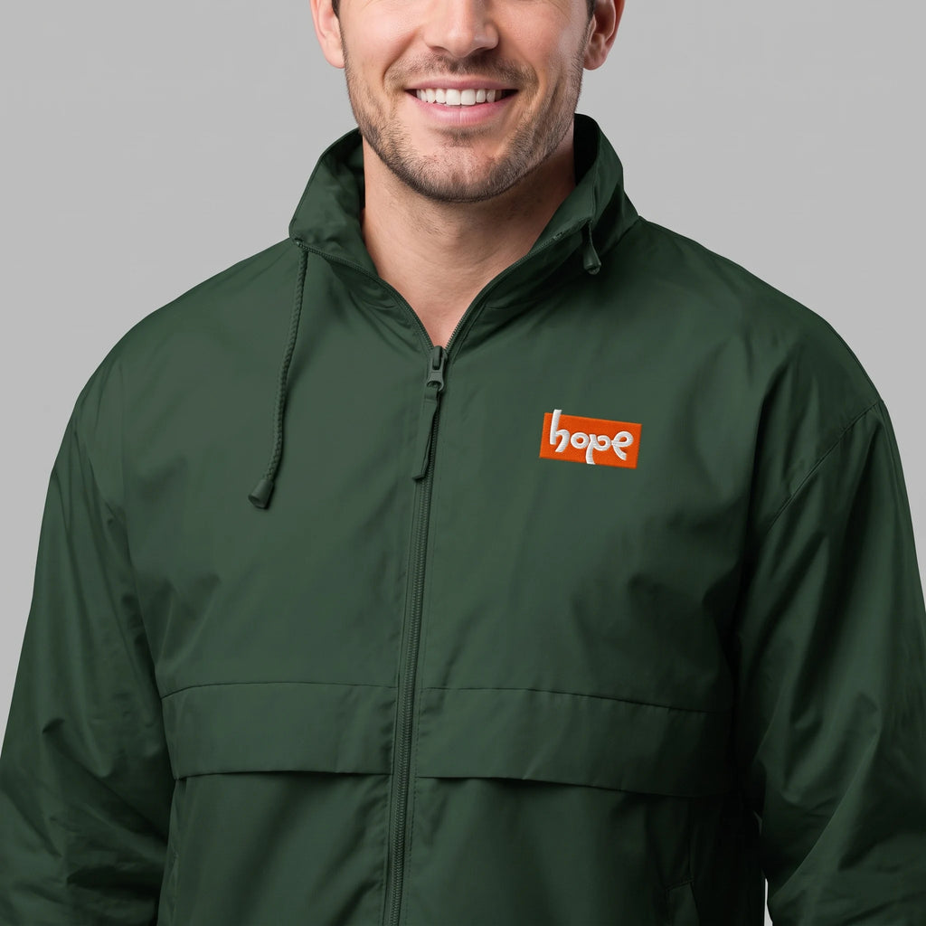 Close-up shot of smiling male model wearing forest green zip-up windbreaker jacket with orange Hope chest logo