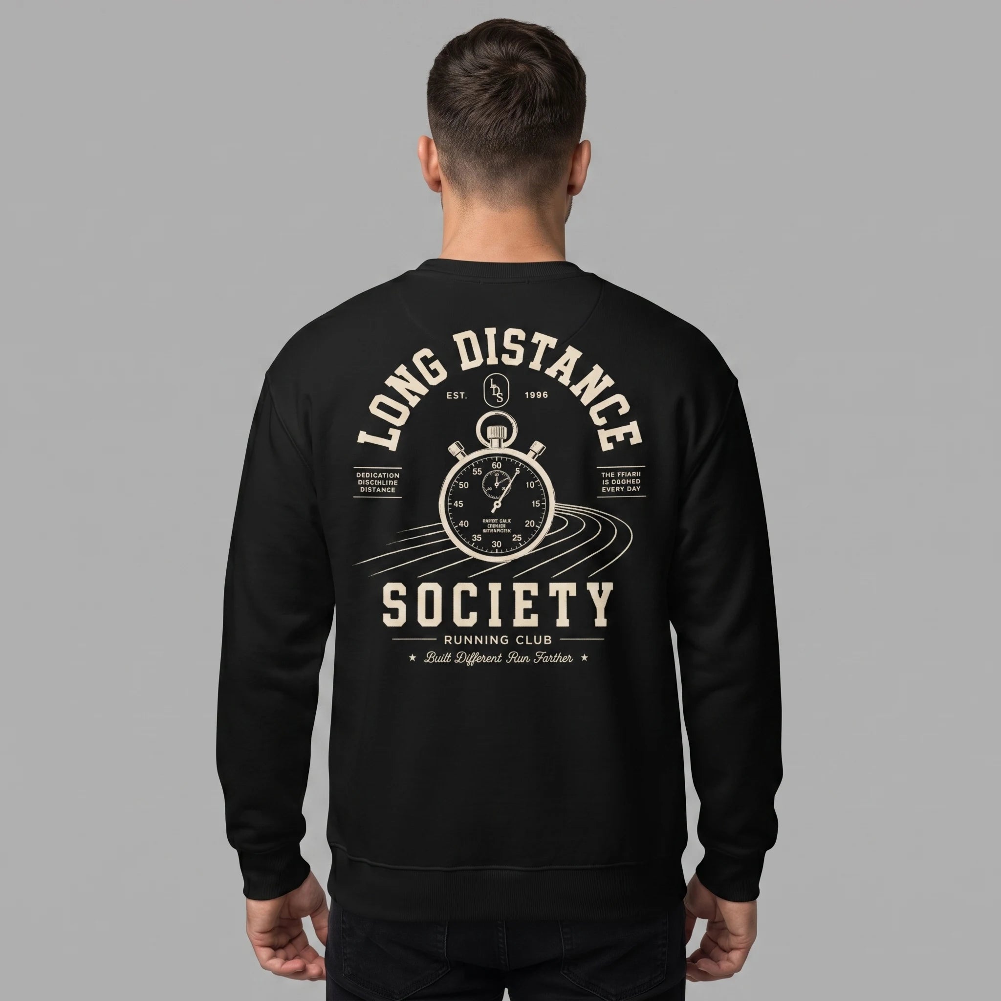 Back view of a male model with short dark hair, standing against a grey background wearing a black crewneck sweatshirt. The back of the sweatshirt features an off-white graphic of a vintage stopwatch over running track lines, surrounded by the arched text 'LONG DISTANCE' above and 'SOCIETY RUNNING CLUB' below, along with the slogan 'Built Different Run Farther'.