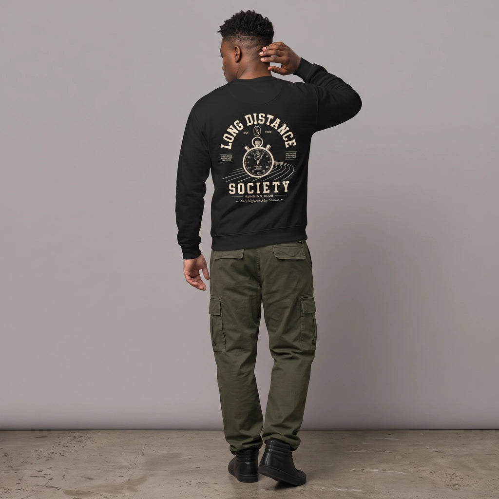Full-length back view of a male model with short dark hair standing against a grey studio background. He is wearing a black crewneck sweatshirt paired with olive green cargo pants and black high-top sneakers. The back of the sweatshirt features an off-white graphic of a vintage stopwatch over running track lanes, surrounded by the text 'LONG DISTANCE SOCIETY RUNNING CLUB'.