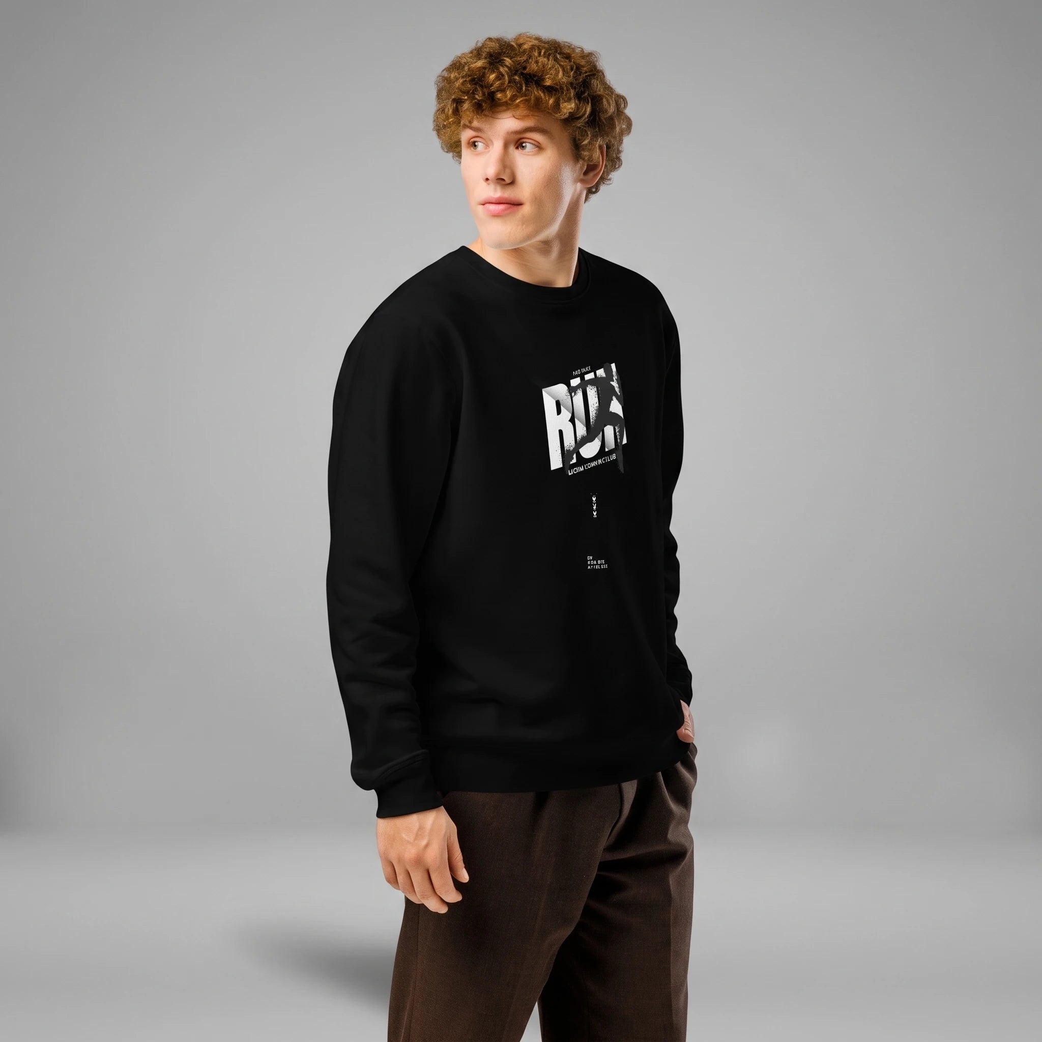 Three-quarter side profile view of a male model with curly brown hair looking to the side against a grey background. He is wearing a black crewneck sweatshirt paired with dark brown trousers, featuring a chest print with the word 'RUN' and a silhouette of a sprinter over the lettering.