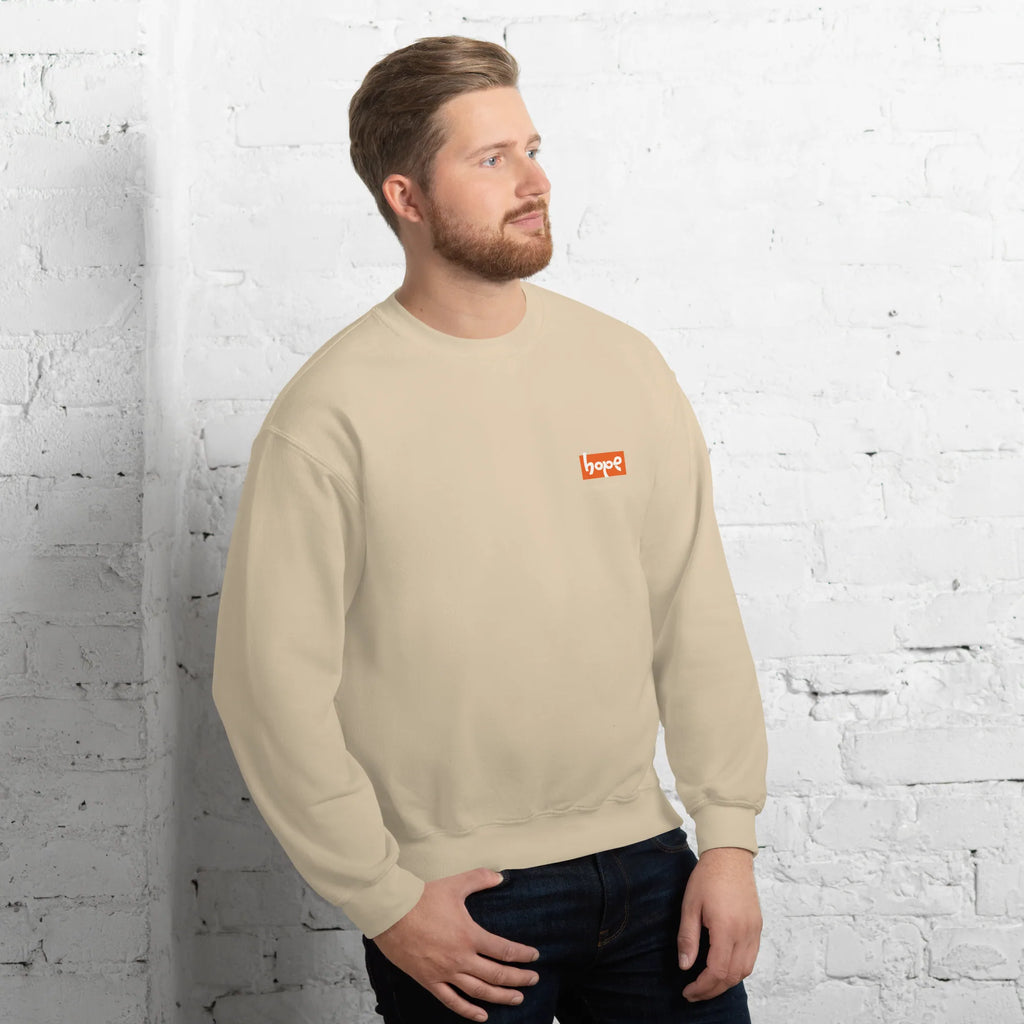 Male model posing in sand beige crewneck streetwear sweatshirt with orange Hope logo against white brick wall