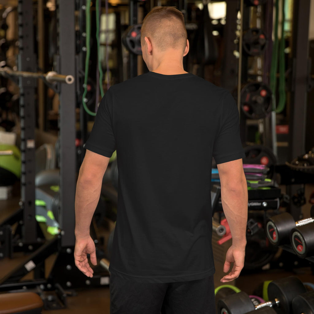 Rear view of a male model standing in a gym, wearing a plain black men's Summerween t-shirt, demonstrating the back fit and length of the spooky summer tee.