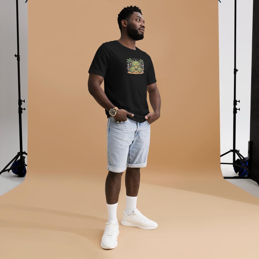 Full-body studio shot of a male model wearing a black men's Summerween graphic t-shirt with a watermelon pumpkin design. He is styled in a casual summer outfit with light denim shorts, white socks, and white sneakers, standing in front of a beige photography backdrop.
