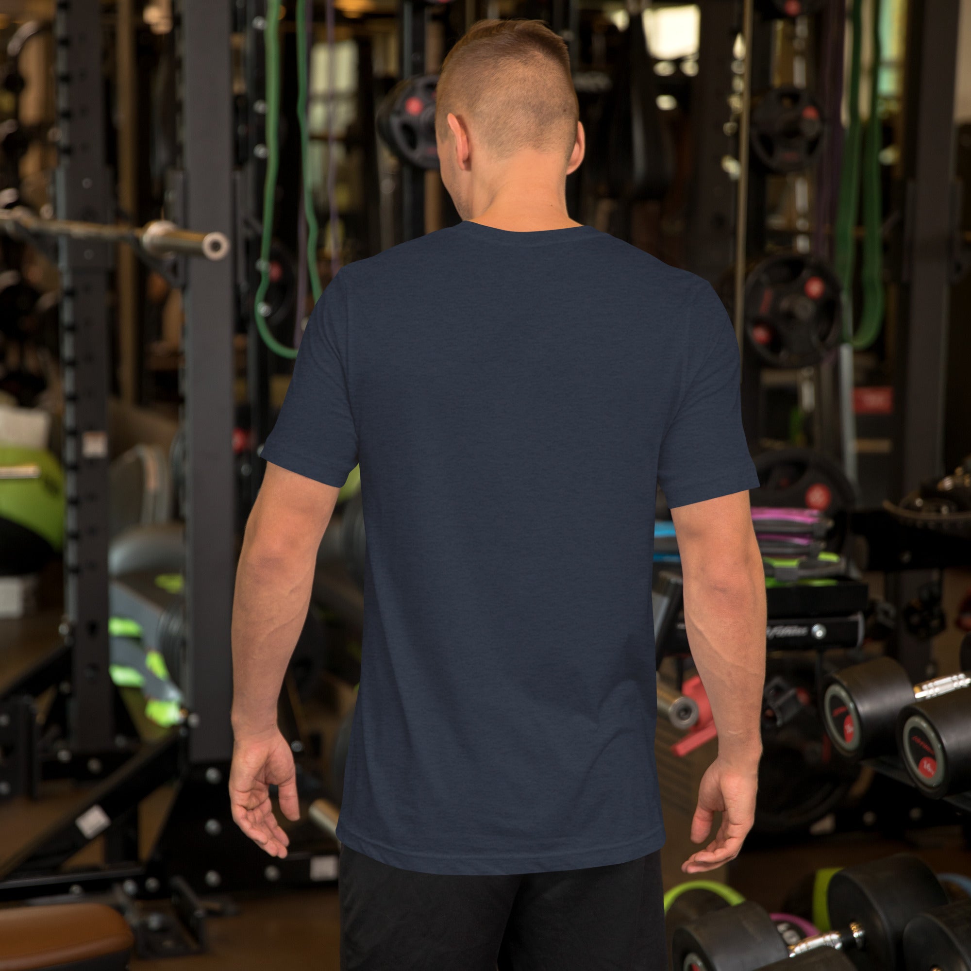 A man in a navy blue Summerween t-shirt, seen from behind, standing in a gym with fitness equipment.