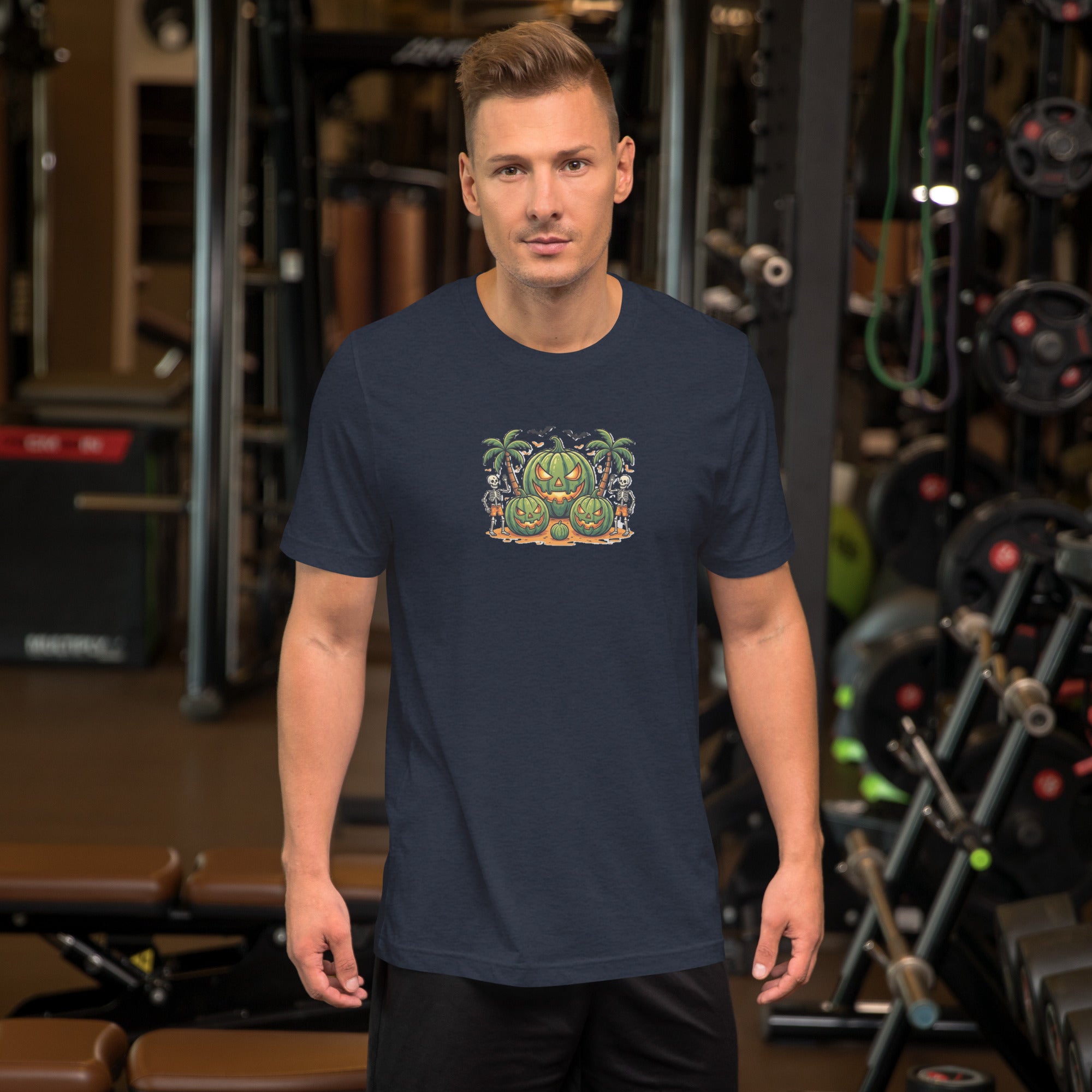 Front view of a male model standing in a gym, wearing a navy blue men's Summerween graphic t-shirt featuring a tropical watermelon jack-o'-lantern and skeletons design.