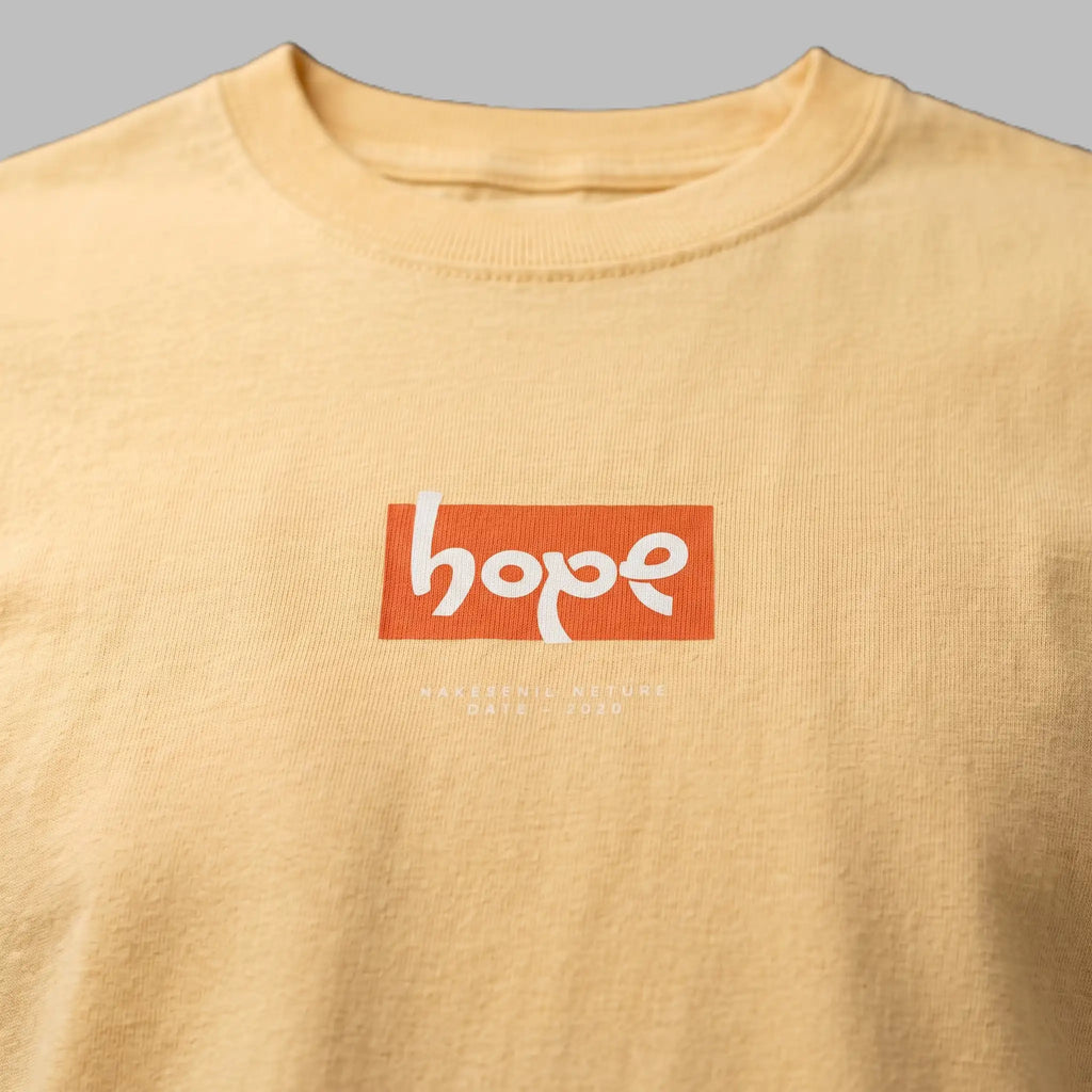 Close-up of a pastel yellow crewneck t-shirt featuring an orange 'hope' box logo graphic print on the chest.