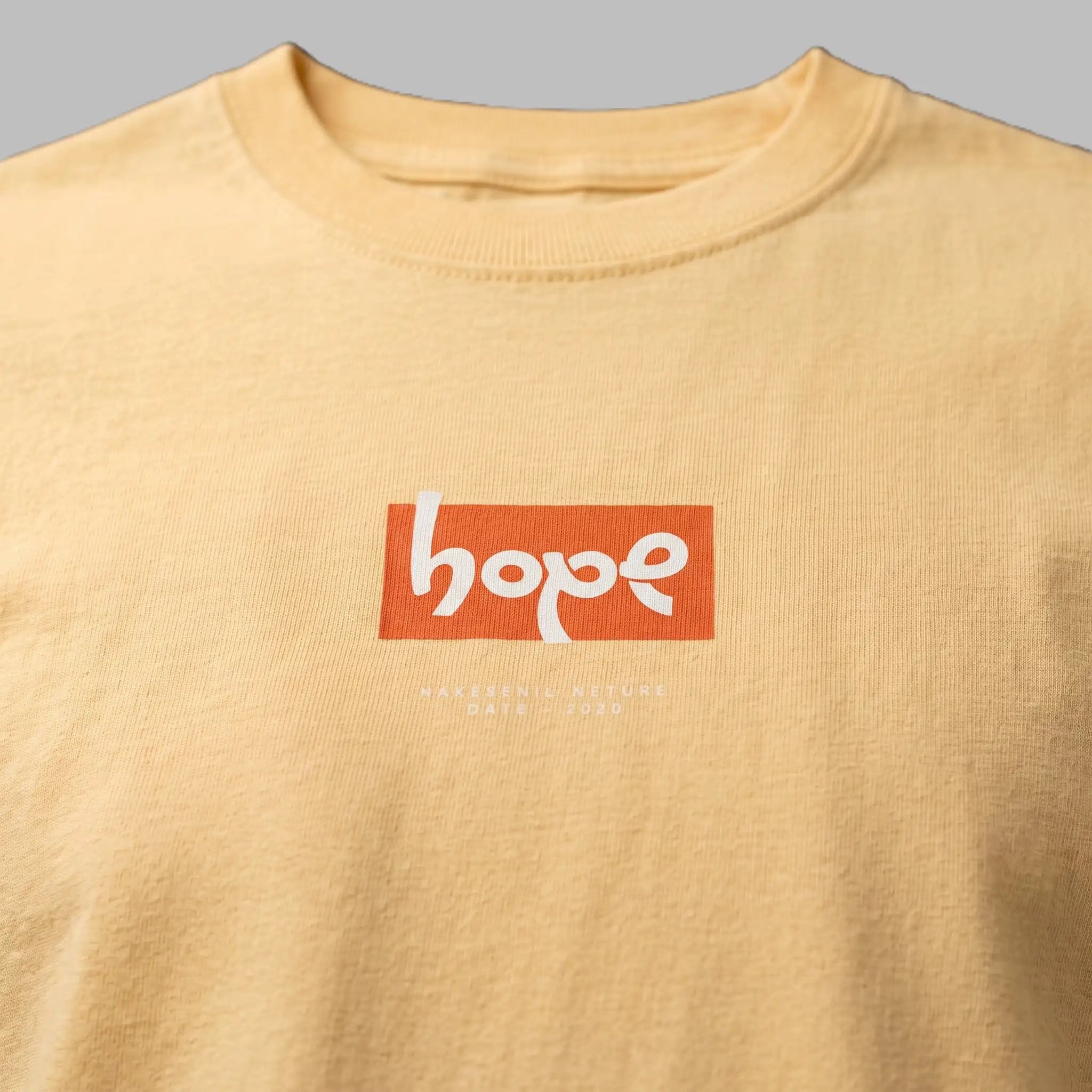 Close-up of a pastel yellow crewneck t-shirt featuring an orange 'hope' box logo graphic print on the chest.