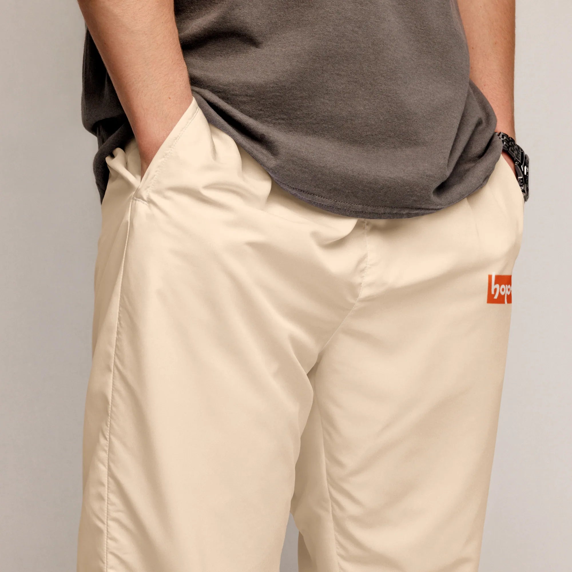 Close-up of male model wearing sand beige track pants showing side pocket and orange Hope logo detail