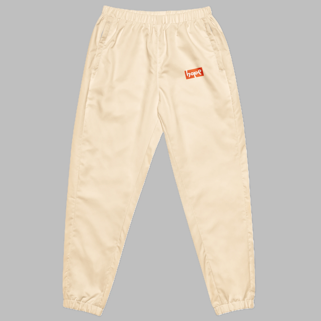 Sand beige unisex streetwear track pants with orange Hope logo and elastic cuffs front view