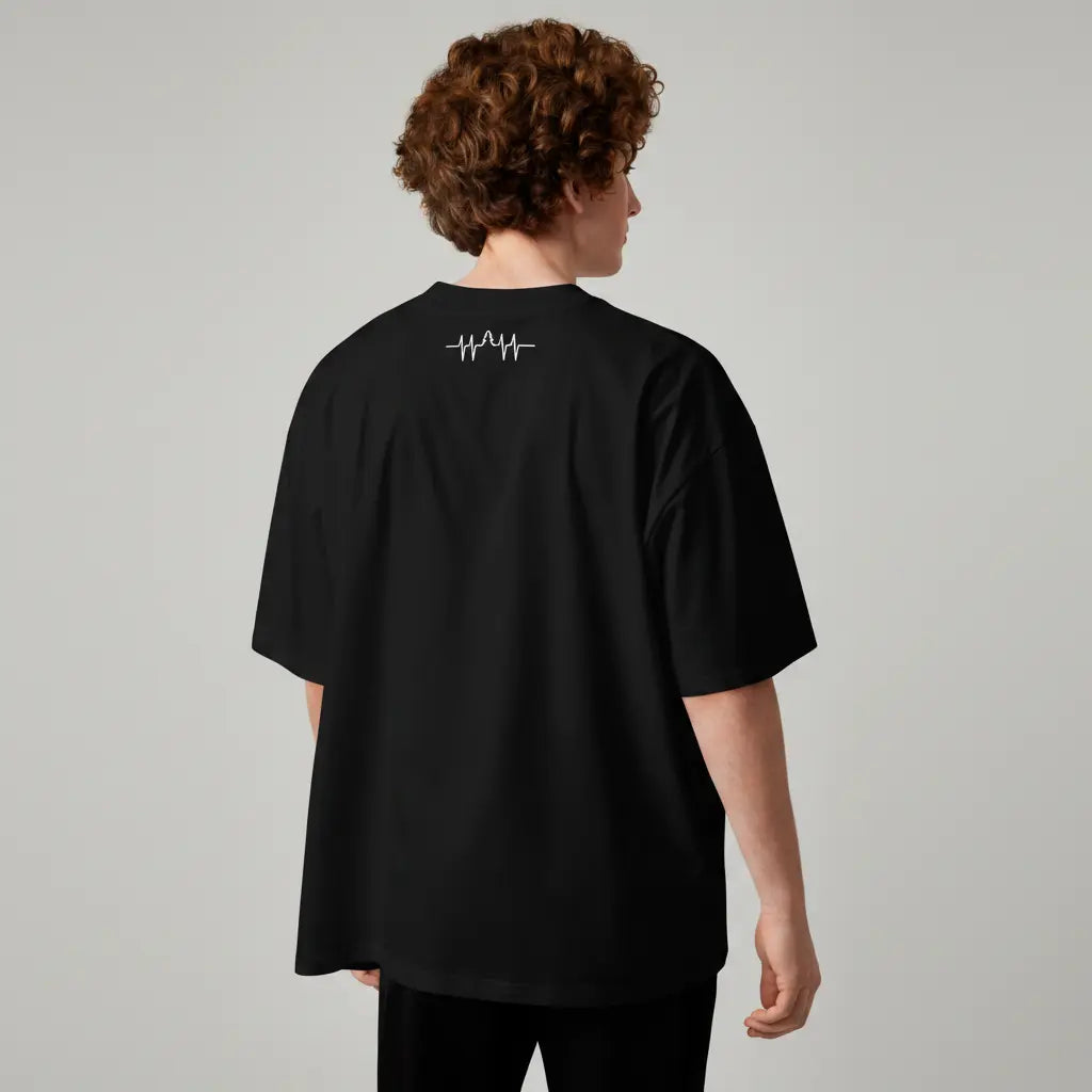 Back view of a man wearing an oversized black organic cotton t-shirt. The shirt features a minimalist white heartbeat and tree line graphic on the upper back.
