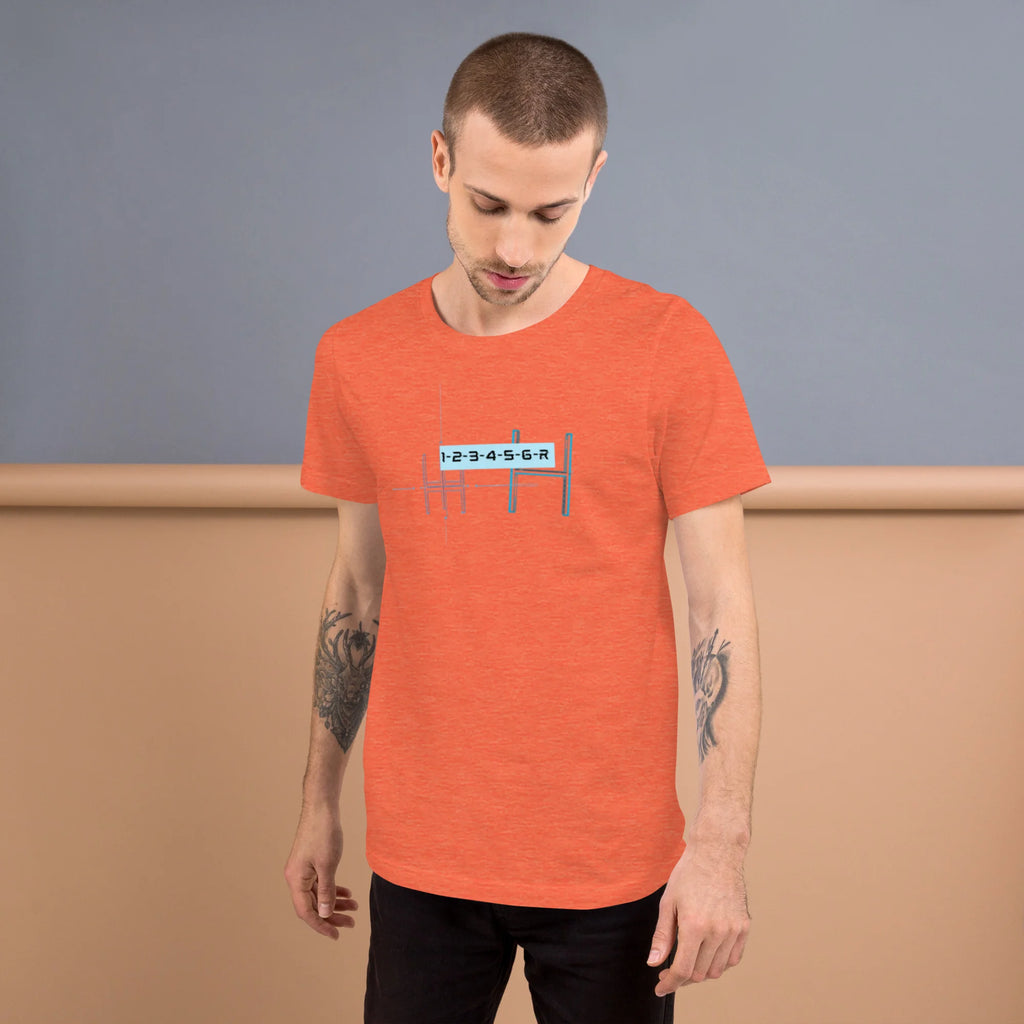 Male model with arm tattoos wearing a heather orange graphic t-shirt featuring a detailed 6-speed manual transmission blueprint shift pattern diagram