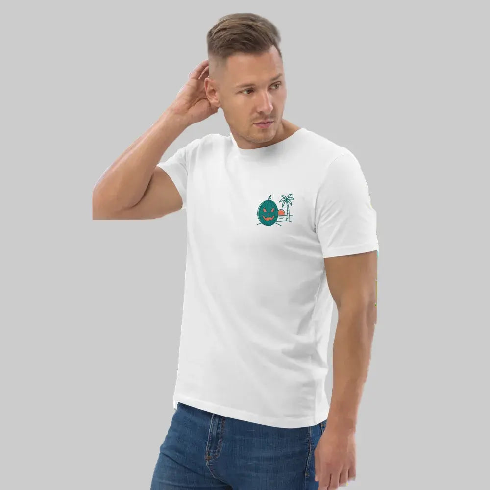 Half-body portrait of a male model posing casually with one hand behind his head, wearing a white organic cotton unisex t-shirt that features a Summerween tropical green jack-o-lantern and palm tree graphic on the left chest, paired with blue jeans against a light grey background.