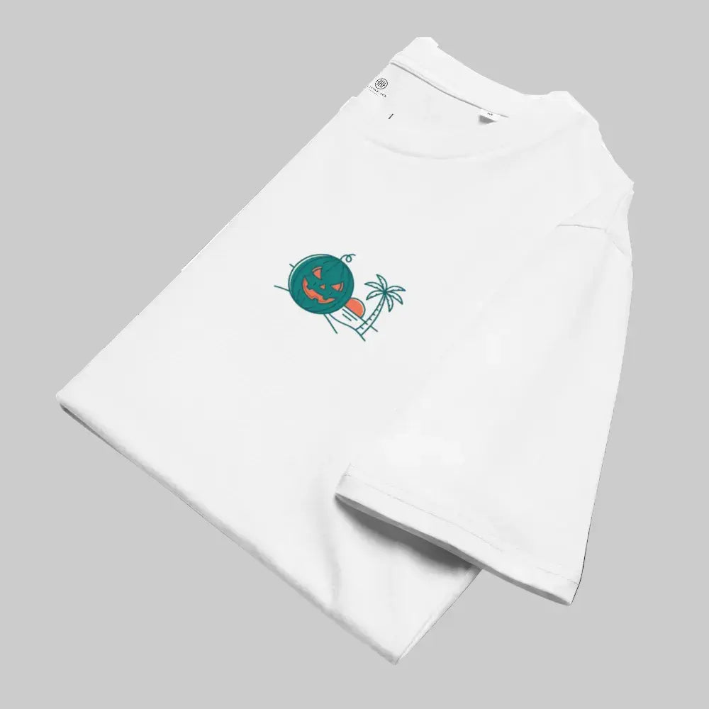 Folded white organic cotton unisex t-shirt placed diagonally on a light grey background, showcasing the Summerween tropical green jack-o-lantern, palm tree, and sunset graphic on the chest.