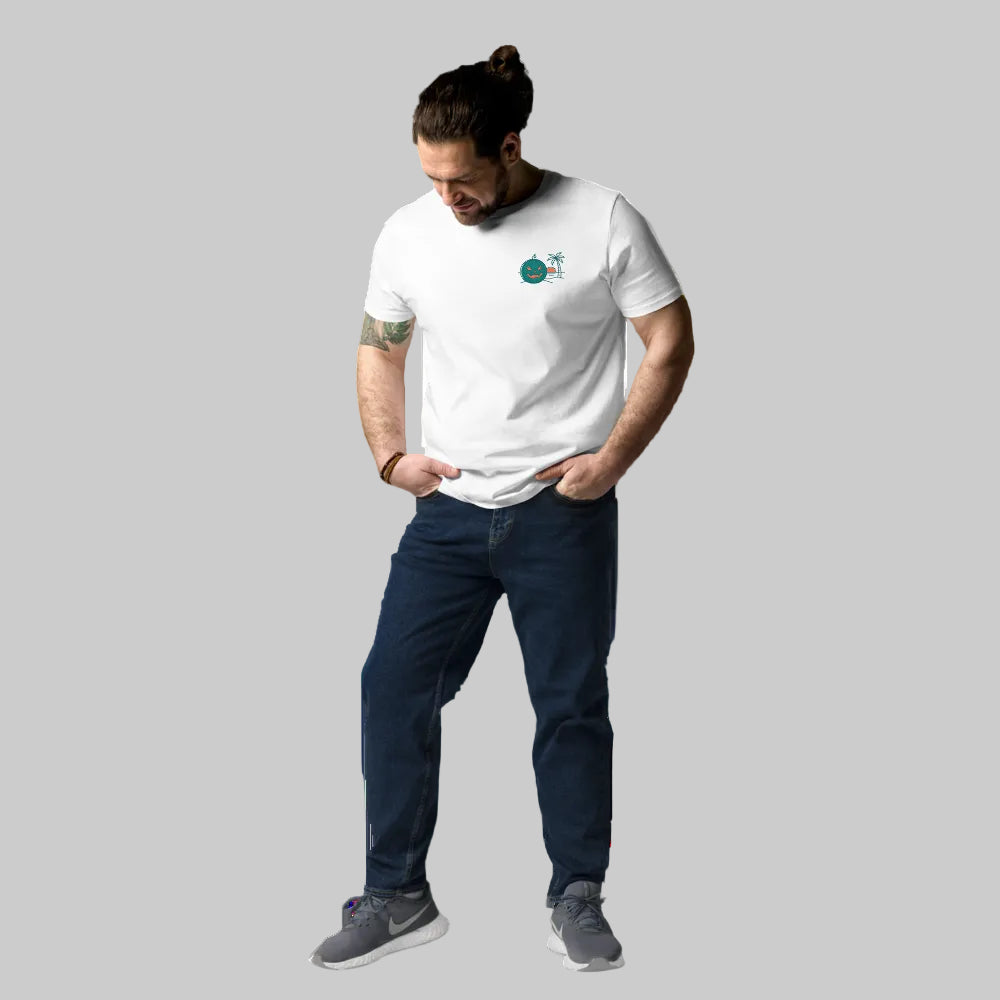 Full-body shot of a male model wearing a white organic cotton unisex t-shirt featuring a Summerween tropical green jack-o-lantern and palm tree graphic on the left chest, paired with blue jeans.
