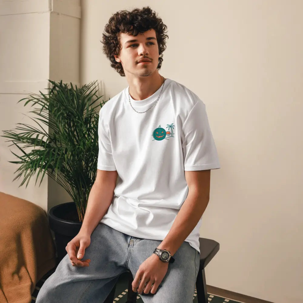 Male model wearing a white organic cotton unisex t-shirt with a Summerween tropical green jack-o-lantern and palm tree graphic on the left chest.