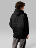 Back view of a model wearing a black oversized hoodie with a wavy graphic print