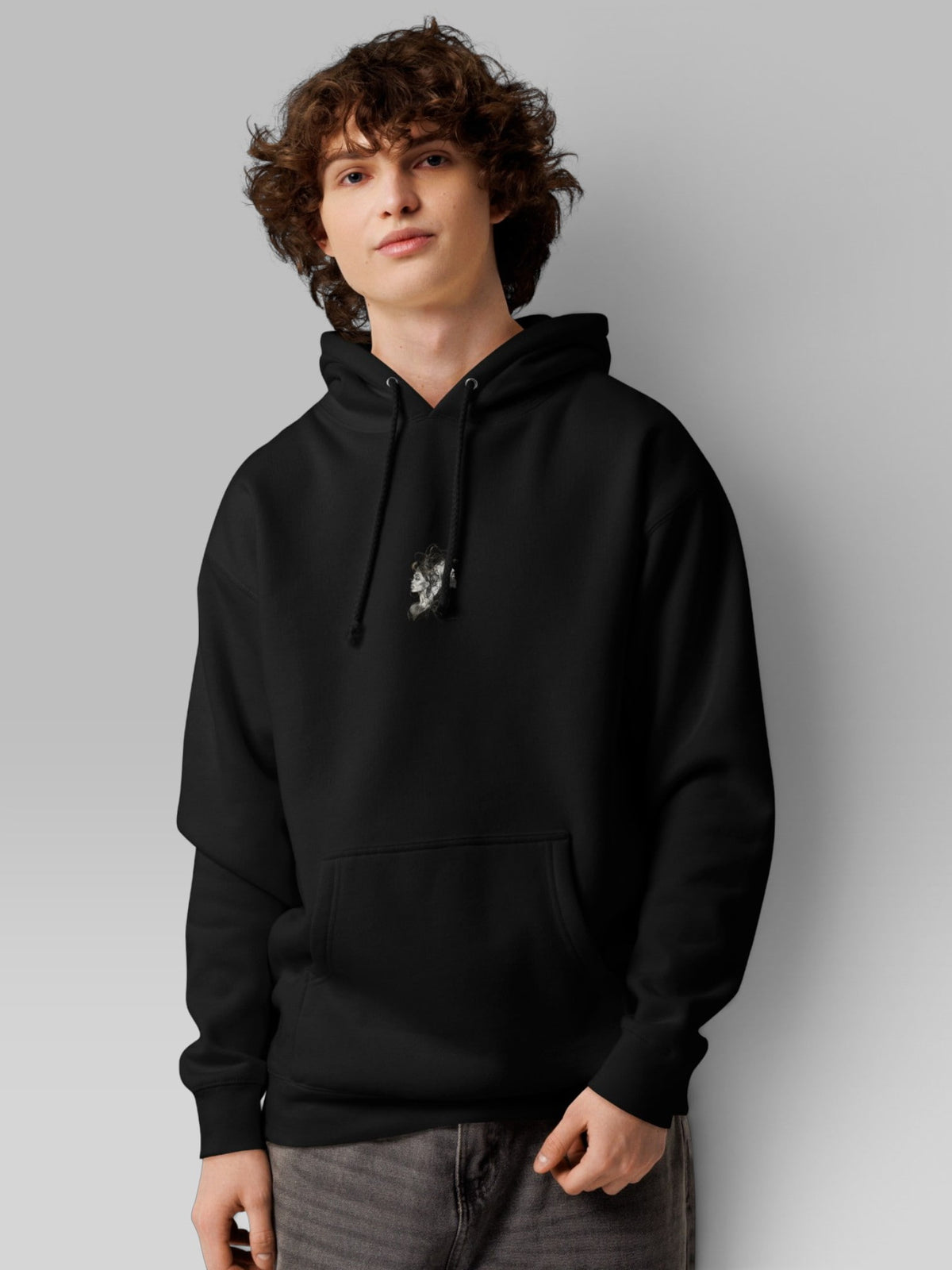 Young male model posing in an oversized black pullover hoodie with pouch pocket and drawstring hood