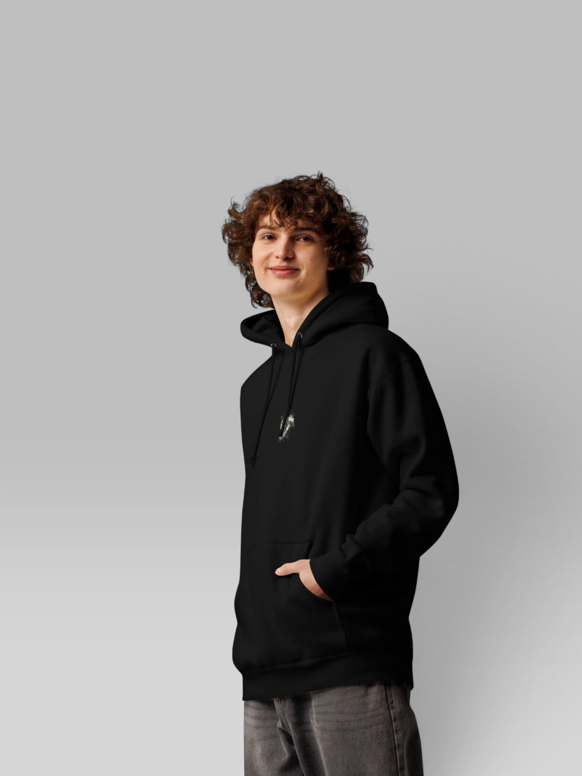 Three-quarter side view of a model in a black oversized pullover hoodie and grey jeans