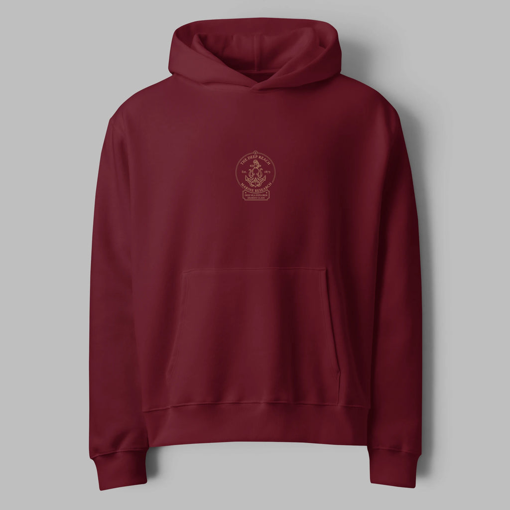 Flat lay front view of an oversized burgundy maroon hoodie featuring a minimal center chest print and pouch pocket